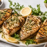 Grilled swordfish steak with salmoriglio sauce plated with lemon halves, parsley, and grilled vegetables