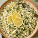 lemon herb rice pilaf with feta in a terracotta bowl, topped with lemon slices and fresh herbs