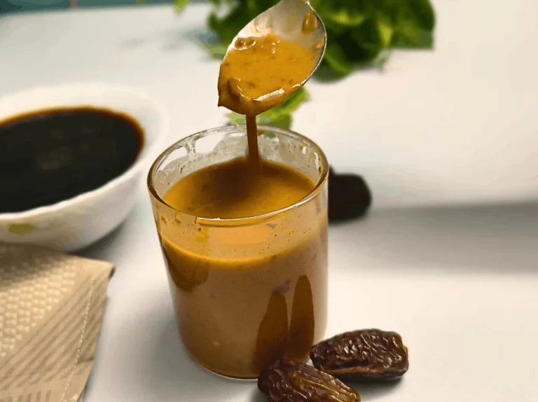 Balsamic date vinaigrette dripping from a spoon into a glass with Medjool dates nearby