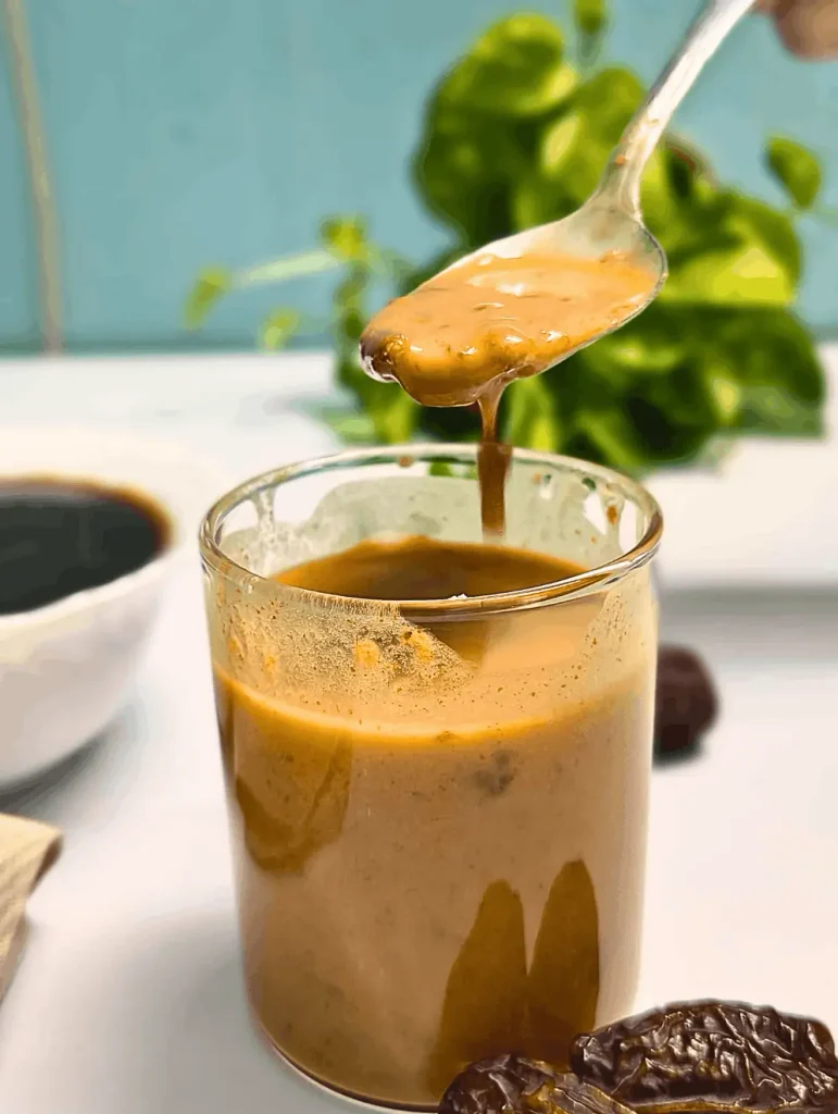 Spoon lifting creamy balsamic date vinaigrette dressing above a glass jar