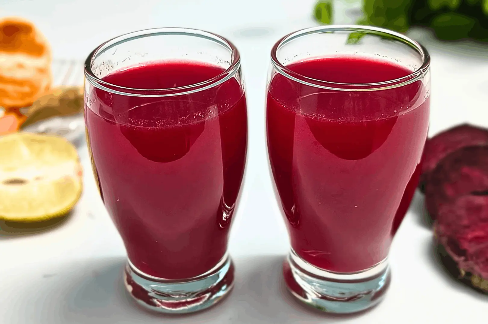 Two glasses of beet ginger juice with orange, lemon, fresh ginger, and beetroot