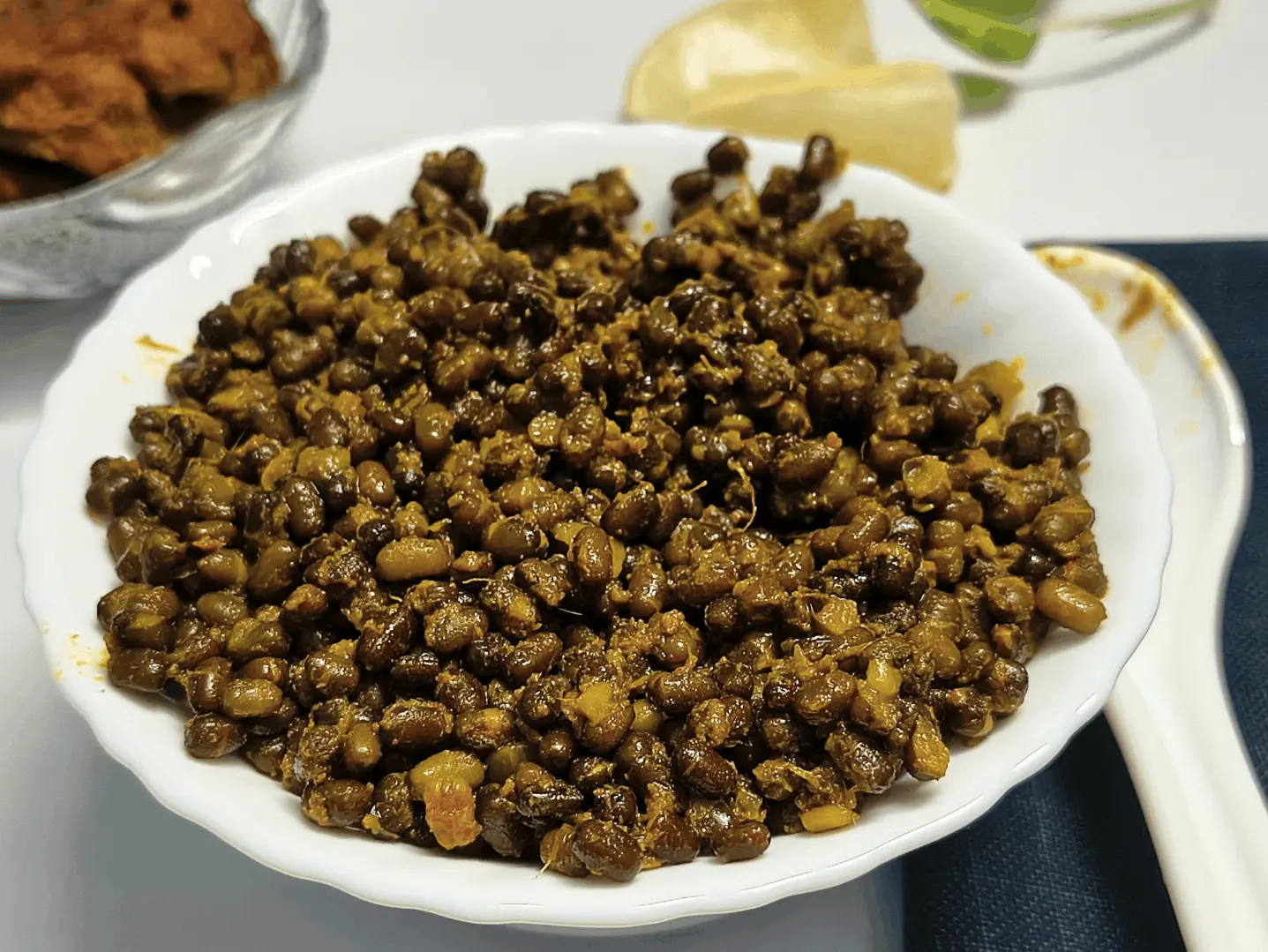A white bowl of cooked black lentils Recipe in a thick, spiced sauce, served with lemon wedges on the side.