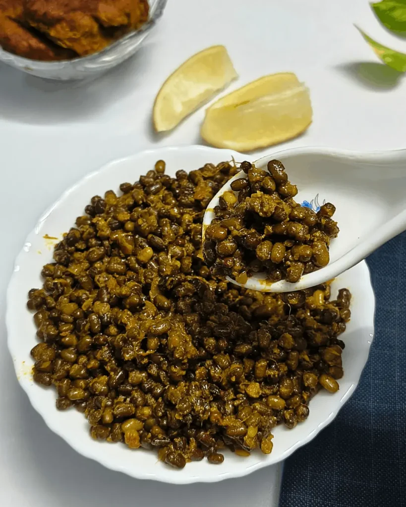 A spoonful of black lentils lifted from a white plate, with lemon wedges and a bowl of chips in the background.