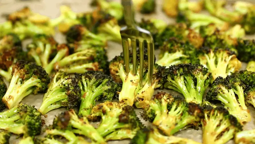 Roasted CAVA fiery broccoli with charred edges on a sheet pan, a fork lifting one floret
