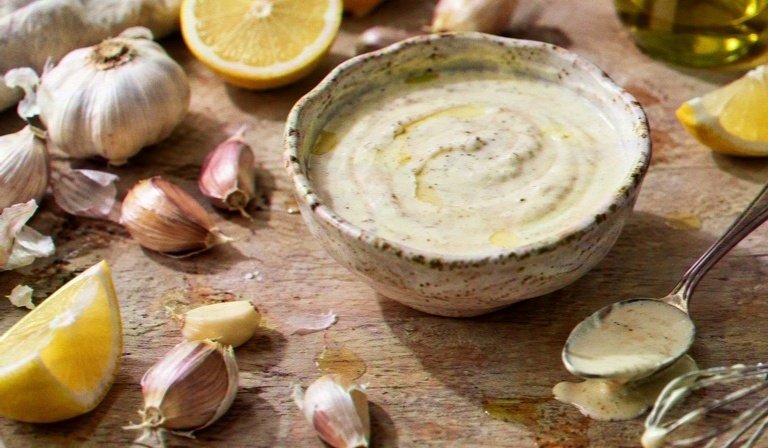 CAVA Garlic Dressing in a creamy sauce bowl with garlic cloves and lemon wedges