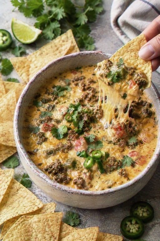 Creamy ground beef queso dip topped with cilantro and jalapeño, with tortilla chips around the bowl