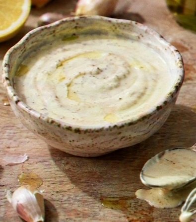 Homemade CAVA Garlic Dressing with garlic cloves, lemon wedges, and a spoon