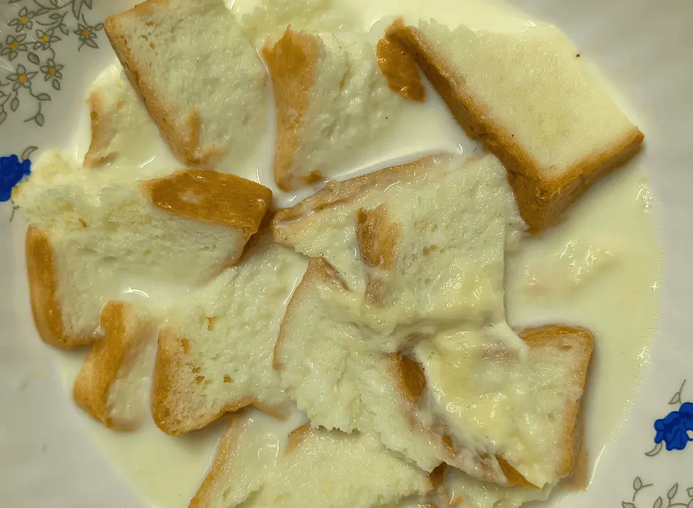 Bread pieces soaking in milk in a floral bowl for caramel bread pudding.