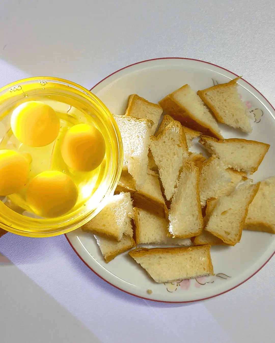 Bowl of eggs next to a plate of bread pieces for caramel bread pudding