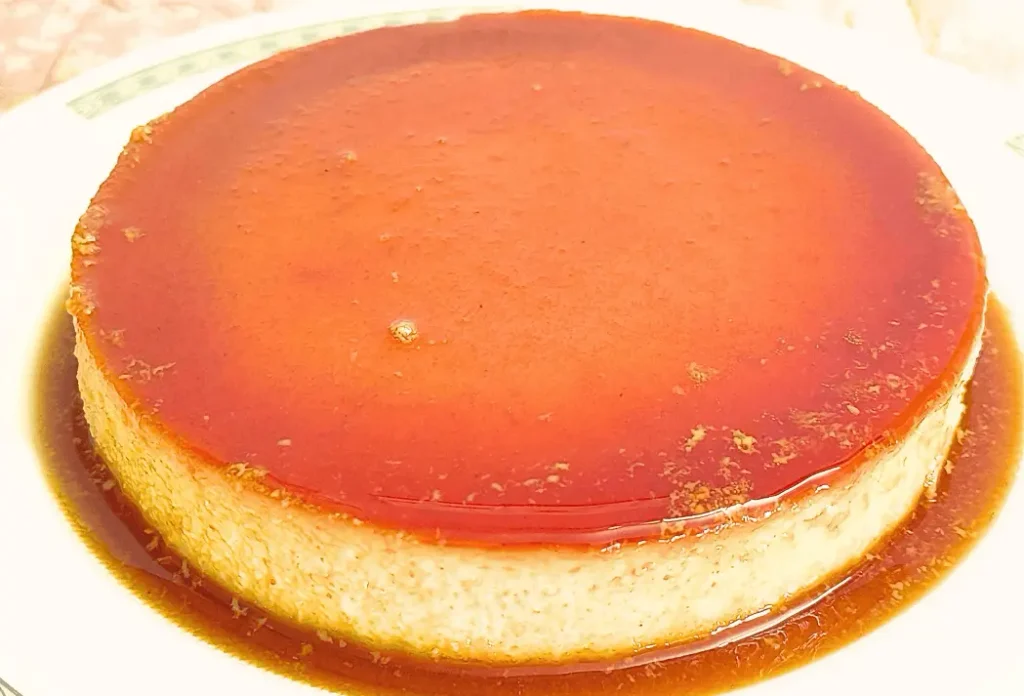 Whole caramel bread pudding with glossy caramel topping and caramel sauce on a white plate.